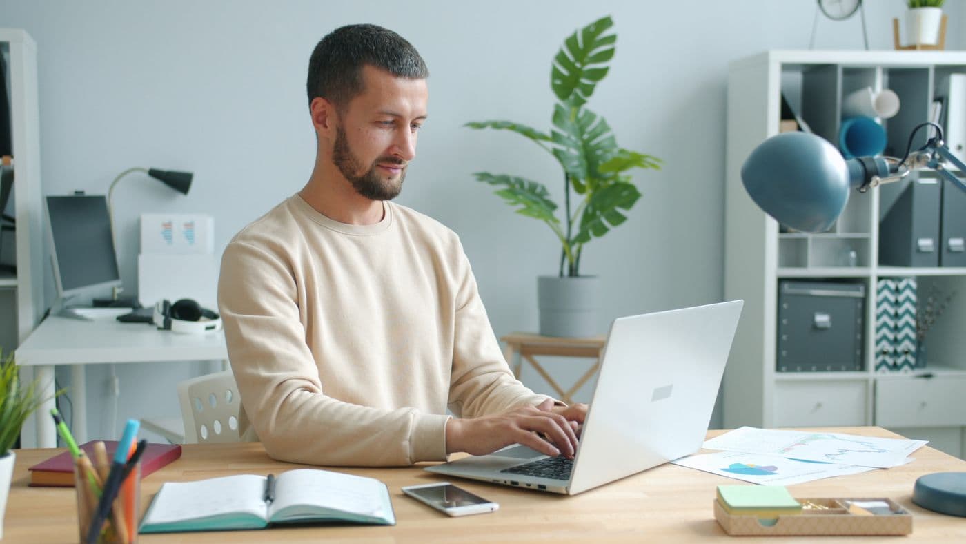 A man working at a laptop with a notebook open beside him